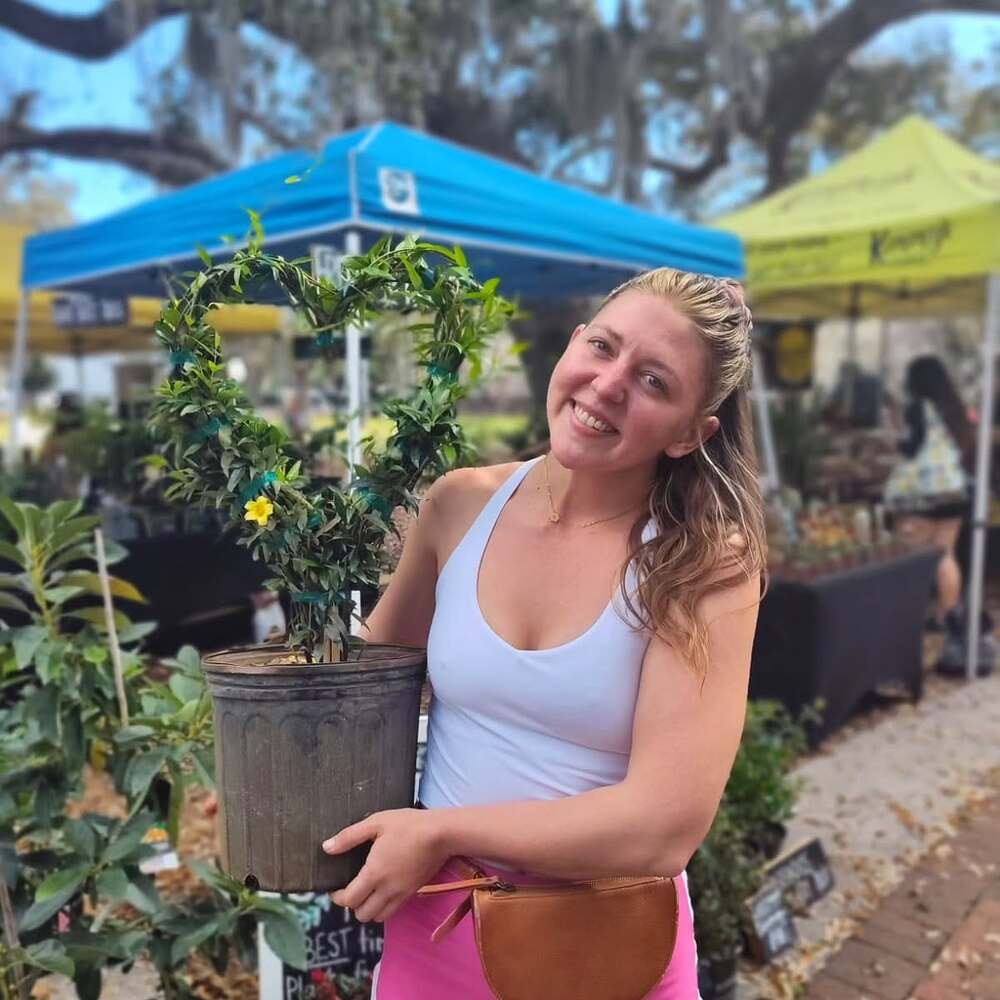a lady holding a flowering yellow jessamine pot