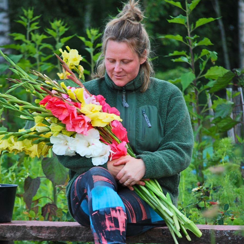 a lady sitting holding bunch of gladiolus in different colors