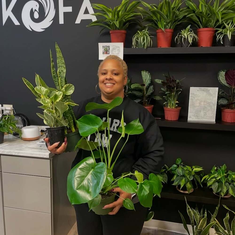 A woman smiles holding indoor plants