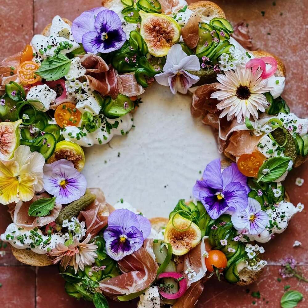 A vibrant wreath-shaped crostini platter decorated with edible flowers and herbs