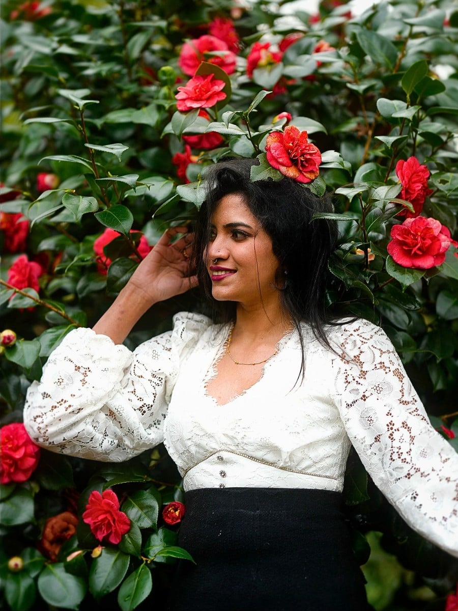 a lady posing with a tree filled with blooming Camellias
