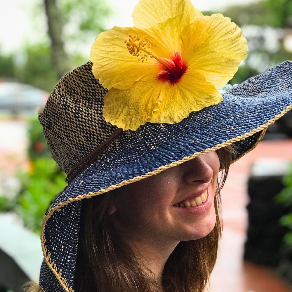 A lady wearing a yellow hibiscus flower on her hat
