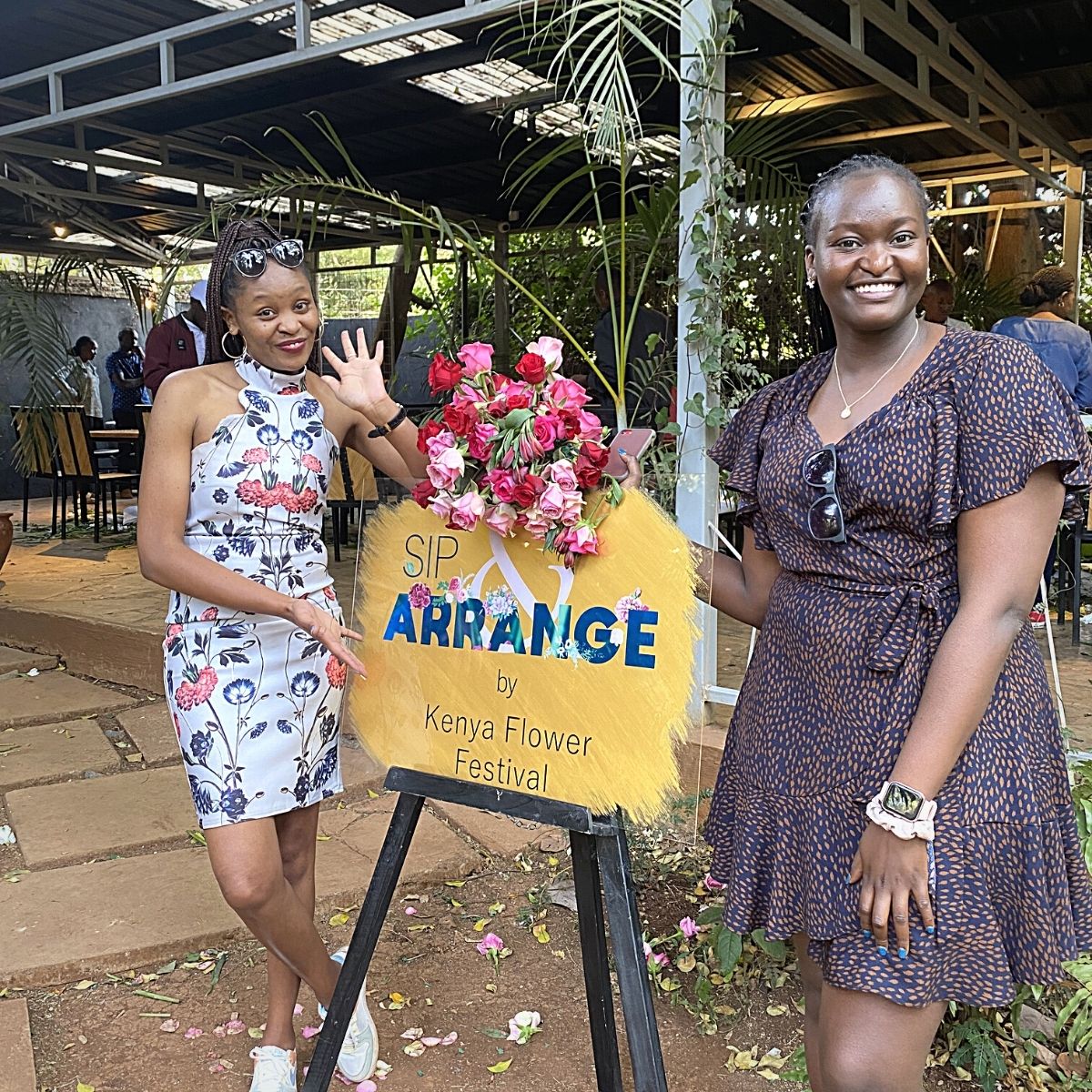 Ladies pose next to Sip and Arrange poster