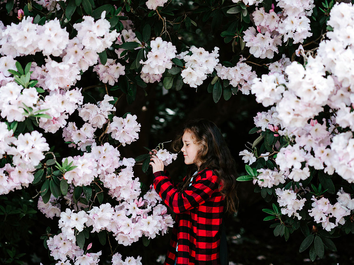 Girl with red and black jacket smelling flowers