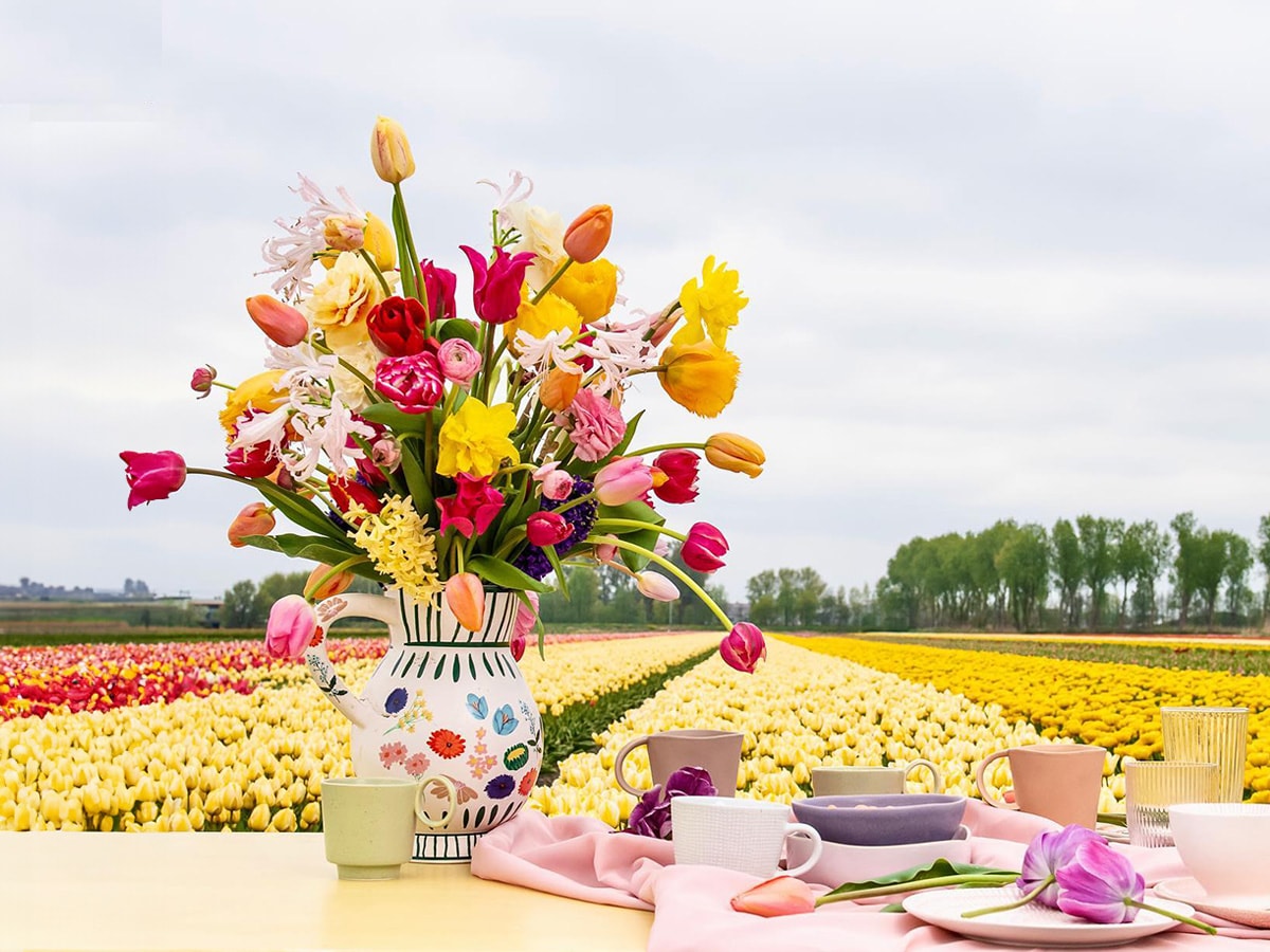 a vase of tulips in multiple colors kept on a table near tulip fields