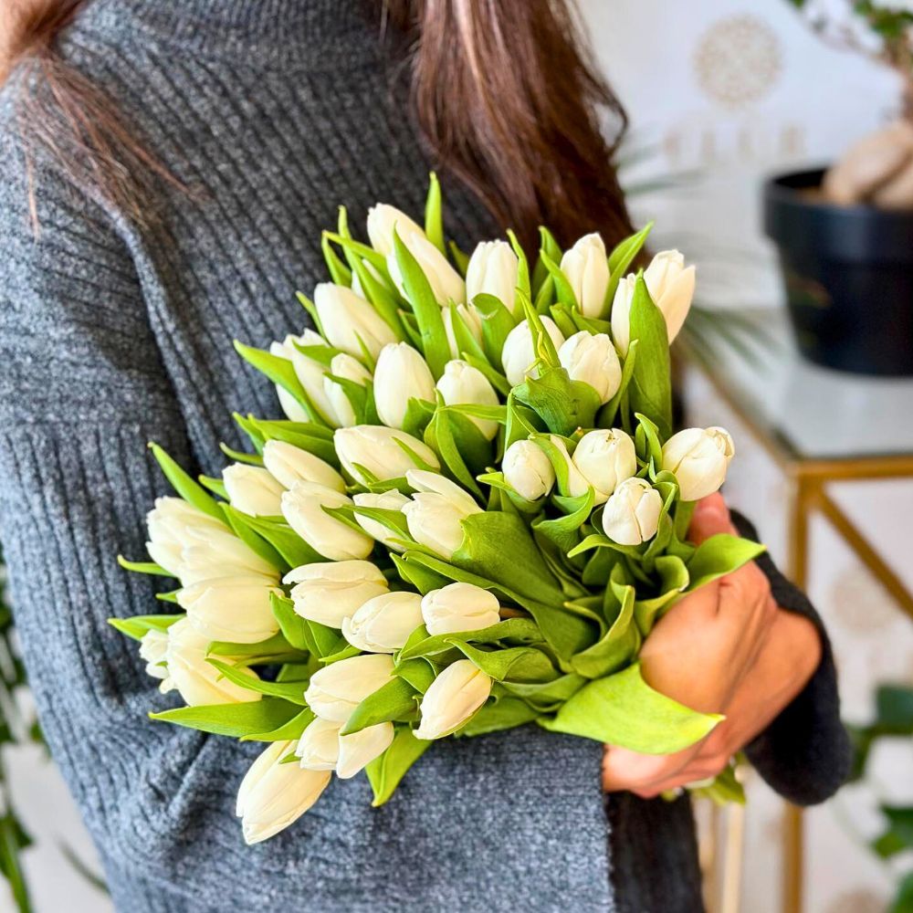 A woman wearing a gray turtleneck sweater holds a large bouquet