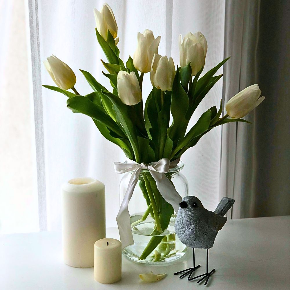 Elegant white tulips in a glass vase with candles and a decorative bird figurine.