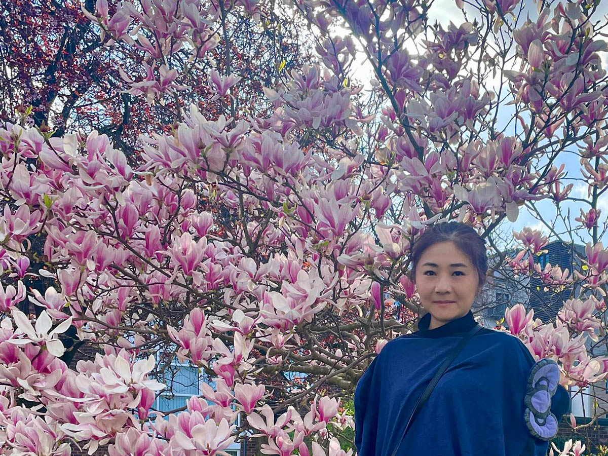 A woman in a navy blue outfit posing in front of a blooming magnolia tree with pink and white flowers.