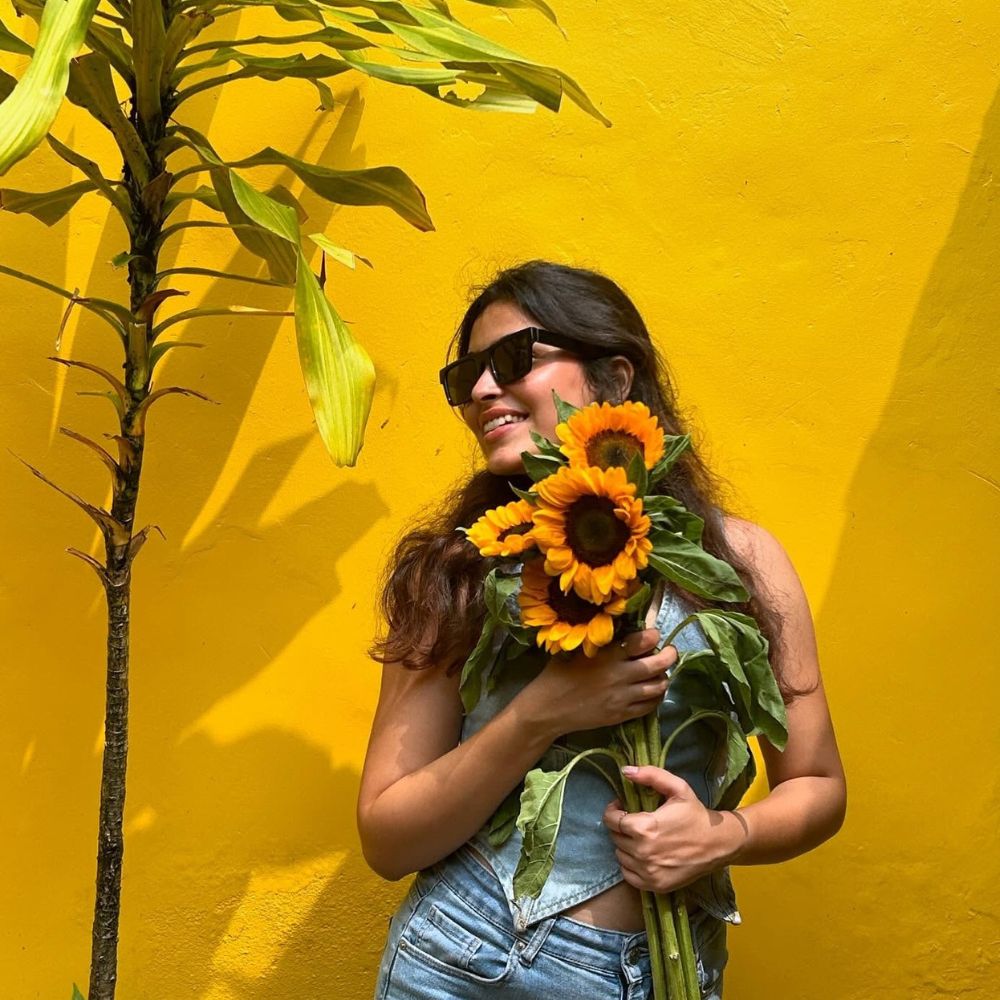 Woman smiles with sunflowers against a yellow wall 