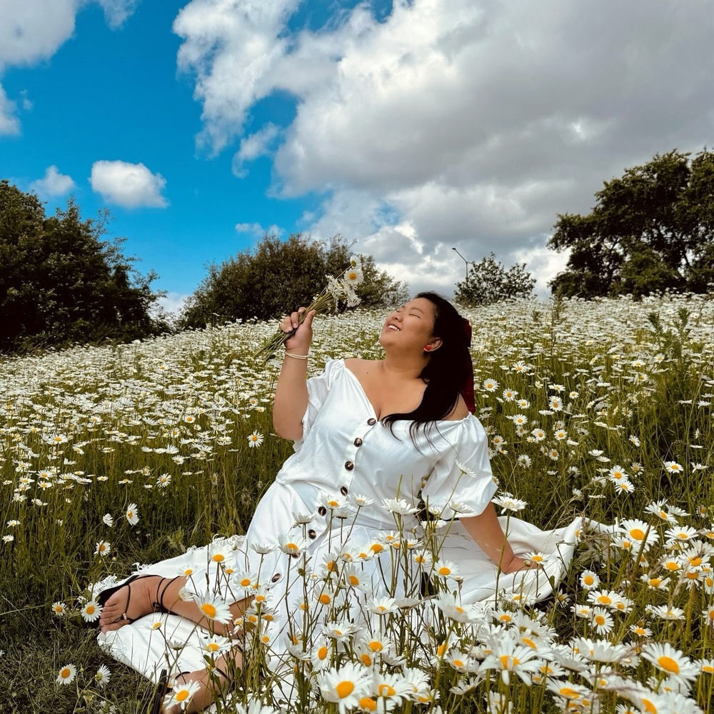 Woman in a white dress, smiling while holding flowers in a field