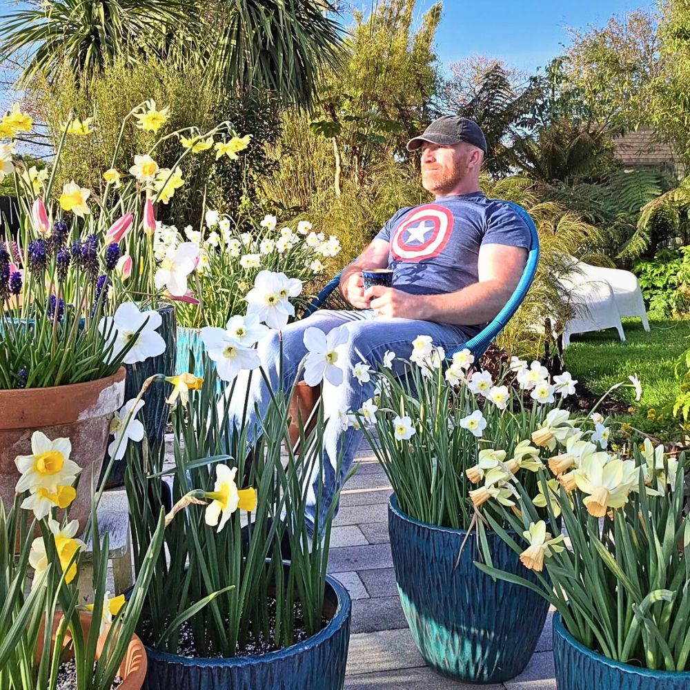 A man having coffee in the midst of potted flowering daffodils